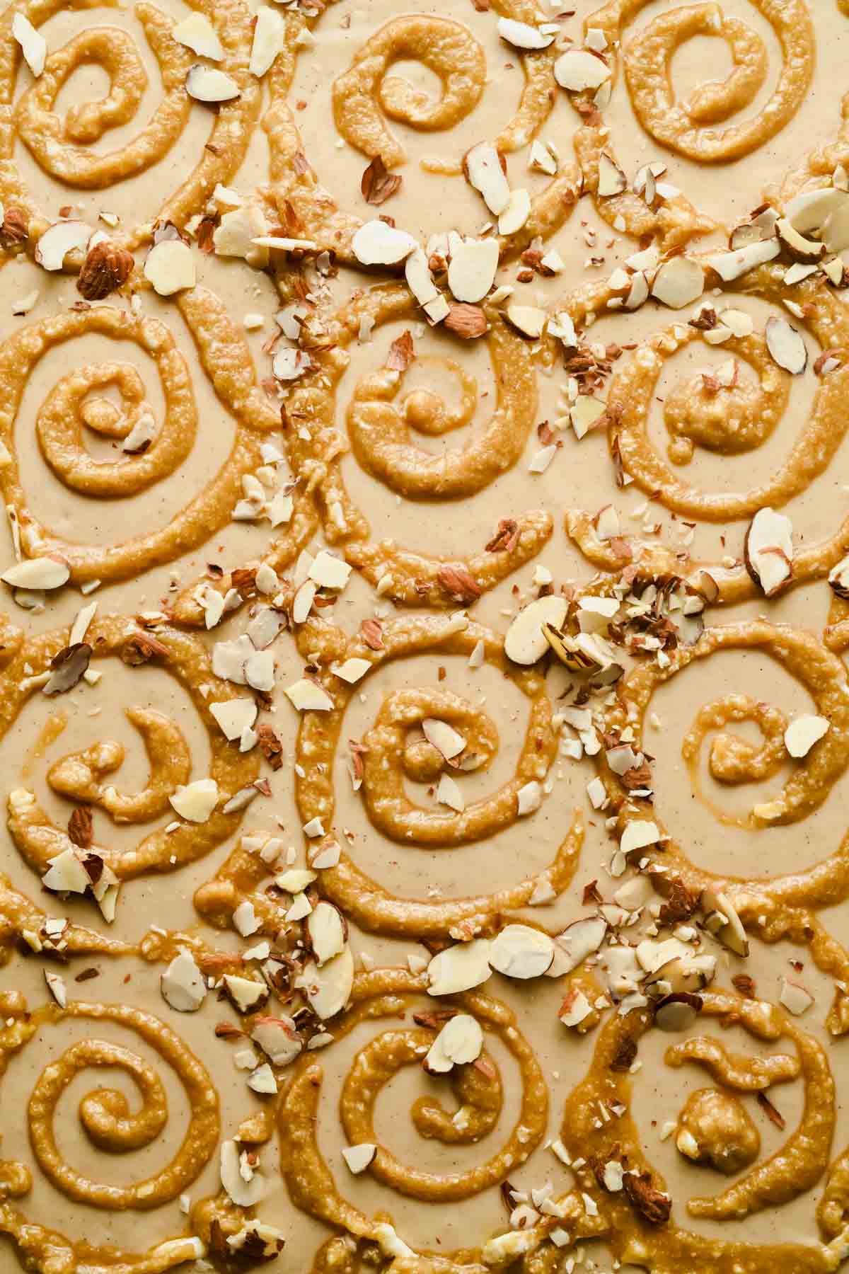 Sheet pan pancake batter topped with piped frangipane swirls and sliced almonds before baking.