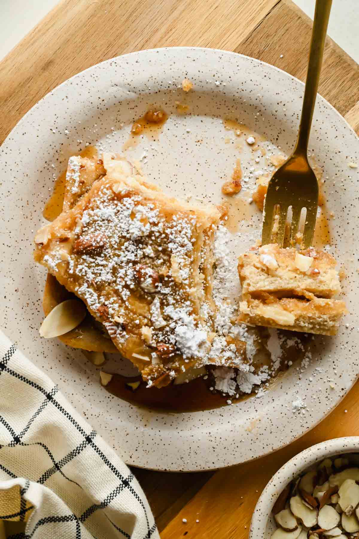 Almond croissant sheet pan pancake squares served with maple syrup and powdered sugar.