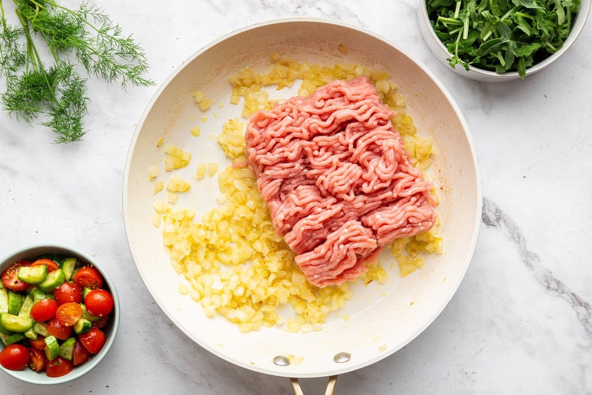 Raw ground turkey in a skillet with sauteed onion and garlic.