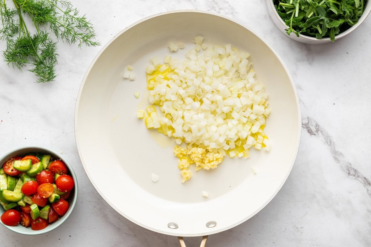 Onion and garlic sauteeing in a white skillet.