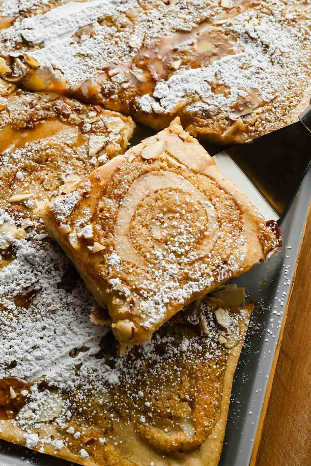 Golden square of sheet pan almond croissant pancake with a frangipane swirl, sliced almonds, and powdered sugar.