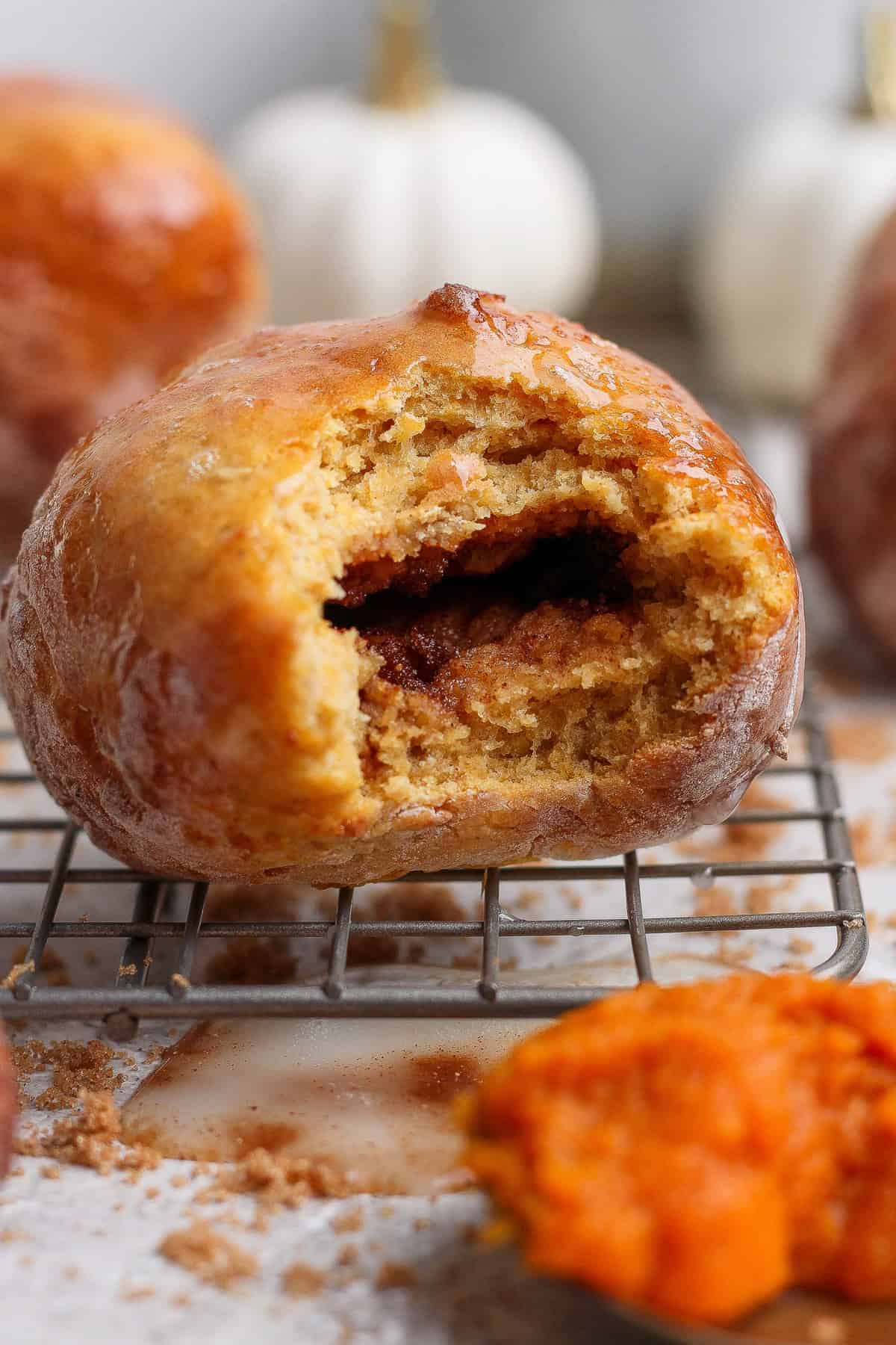 Bitten glazed pumpkin fritter on a wire rack showing the dark brown sugar spice filling inside.