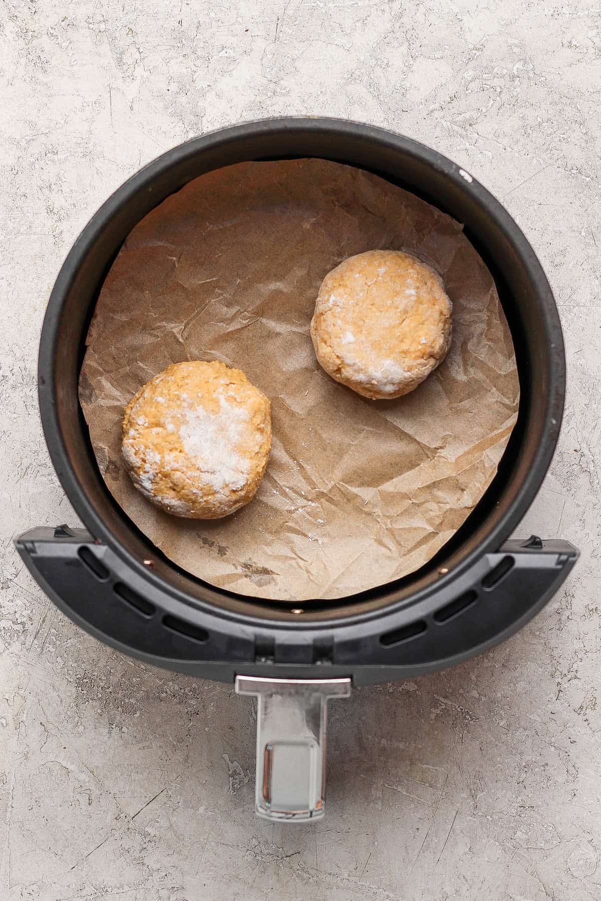 Two shaped uncooked pumpkin fritters on parchment paper inside an air fryer basket.