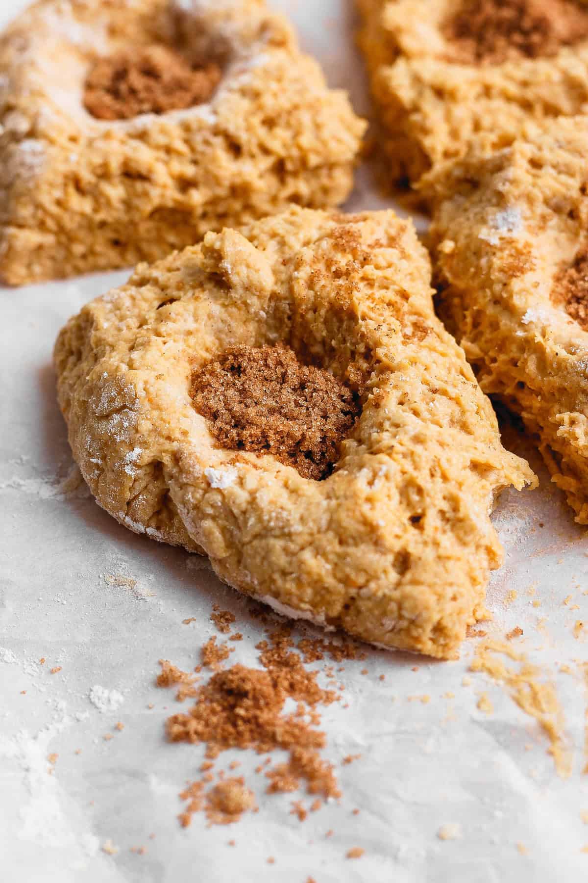 Four pieces of pumpkin fritter dough with wells filled with brown sugar and pumpkin pie spice on a floured surface.