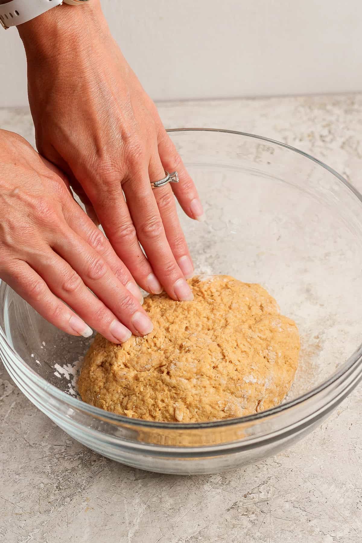 Hands gently kneading pumpkin fritter dough in a clear glass mixing bowl.