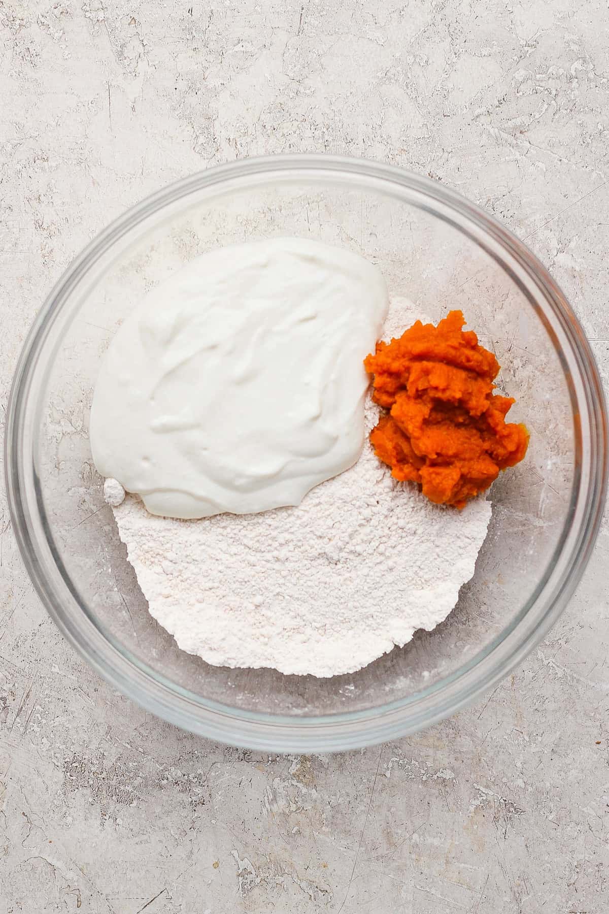 Blended cottage cheese and pumpkin puree added to the flour mixture in a glass bowl.