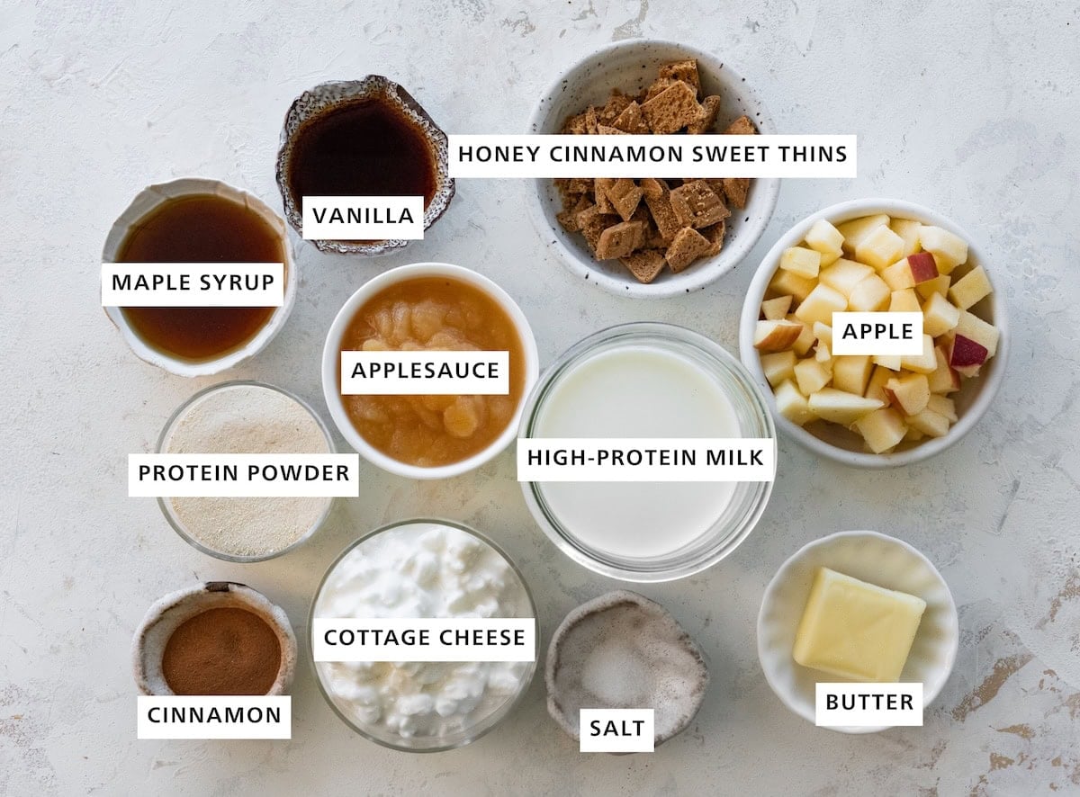 Ingredients measured out for apple pie ice cream: vanilla, honey cinnamon sweet thins, apple, butter, salt, cottage cheese, cinnamon, protein powder, maple syrup, applesauce, and high-protein milk.