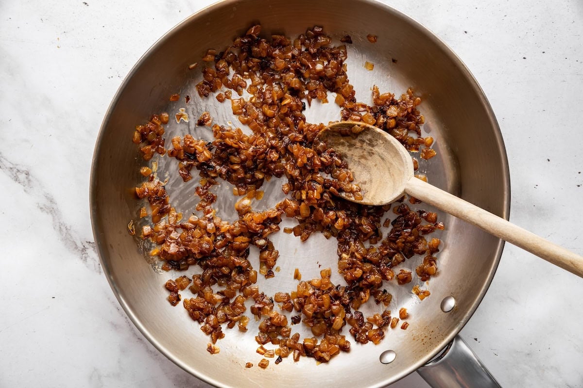 Caramelized onions in a skillet with a wooden spoon.