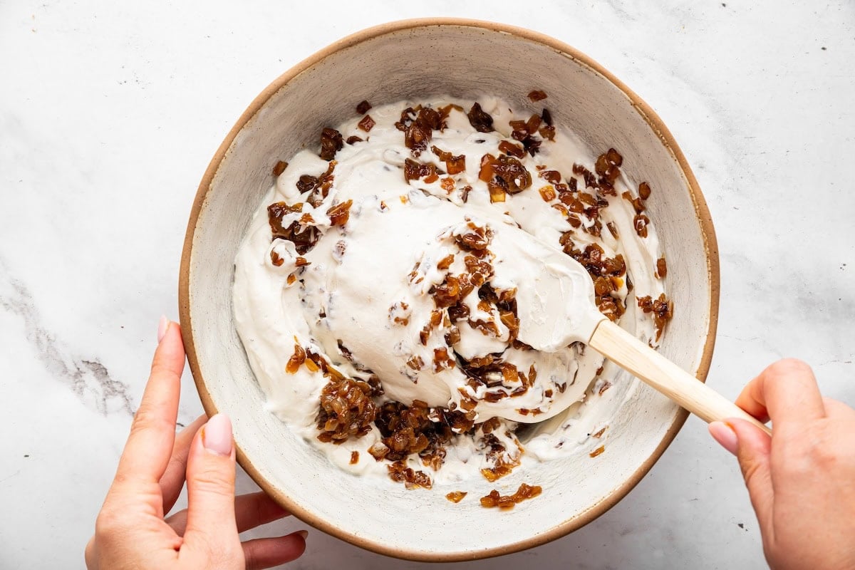A woman's hand mixing the caramelized onions into the creamy cottage cheese mixture.
