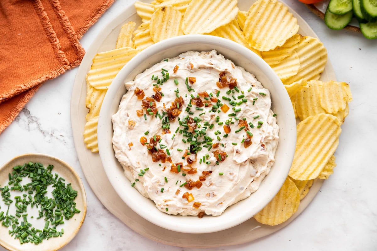 French onion dip served in a bowl topped with fresh chives and caramelized onions. The dip is served with chips.