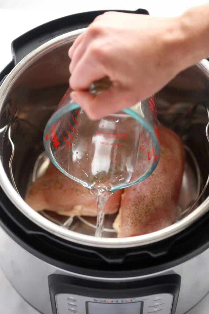 Wondering how to make shredded chicken in the Instant Pot? Look no further! This easy Instant Pot Shredded Chicken recipe is ready in less than 20 minutes, and will easily become a meal-prep staple in your home. water being poured in the instant pot for instant pot shredded chicken.