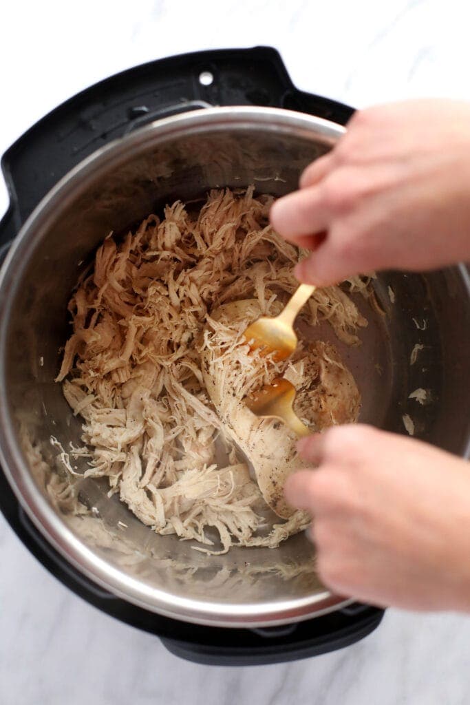 Wondering how to make shredded chicken in the Instant Pot? Look no further! This easy Instant Pot Shredded Chicken recipe is ready in less than 20 minutes, and will easily become a meal-prep staple in your home. two forks shredding instant pot chicken breasts into shredded chicken.