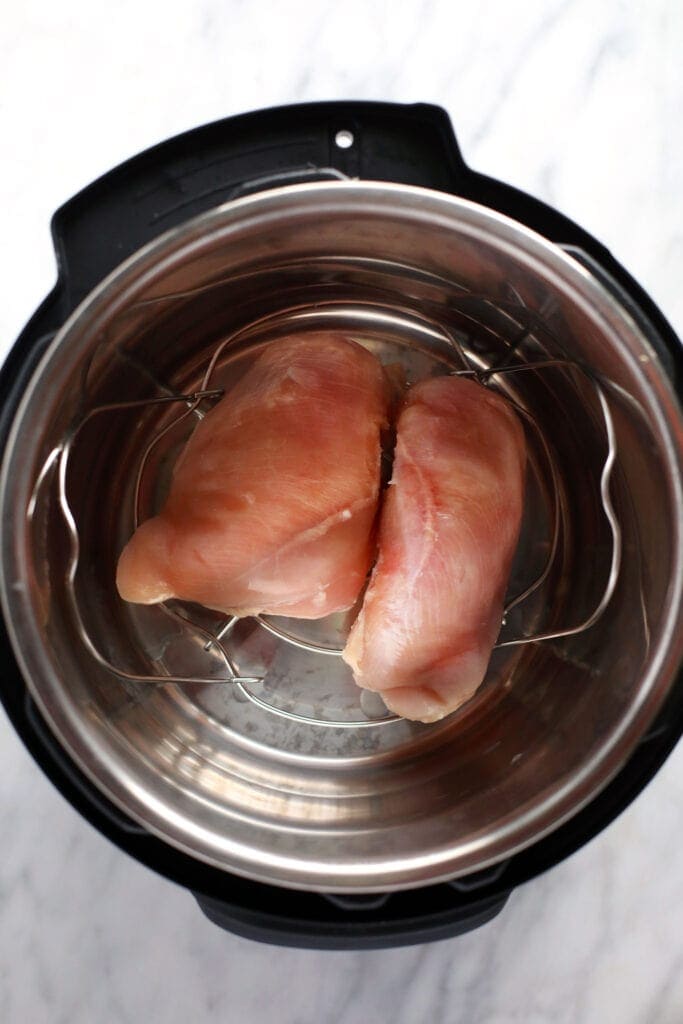 Wondering how to make shredded chicken in the Instant Pot? Look no further! This easy Instant Pot Shredded Chicken recipe is ready in less than 20 minutes, and will easily become a meal-prep staple in your home. raw chicken breasts in the instant pot ready to be cooked and then shredded.